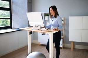 A woman working in an office and using a sit/stand desk.